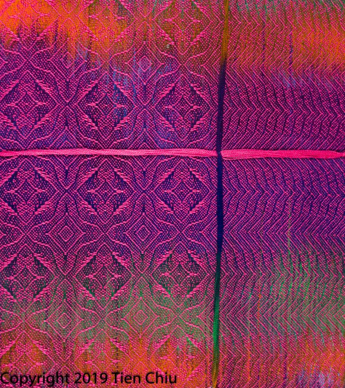 A handwoven sample showing a painted warp in purple, orange, and green painted warp with hot pink weft