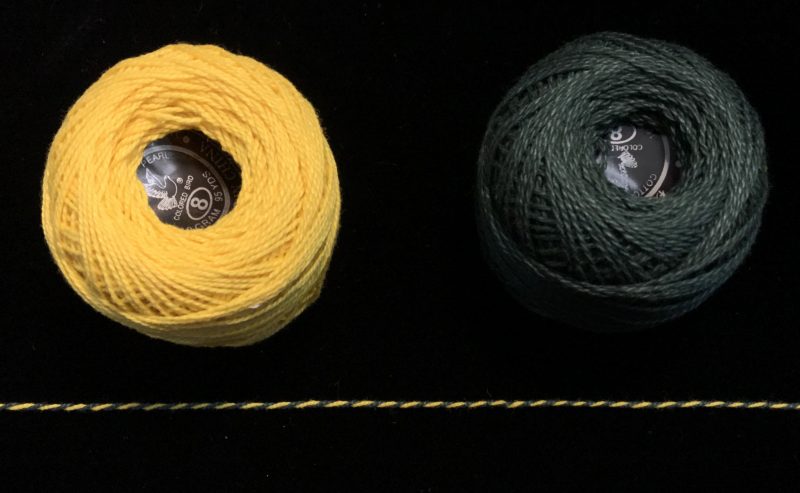 Two balls of yarn, yellow and dark green, which twist together into a barberpole yarn.