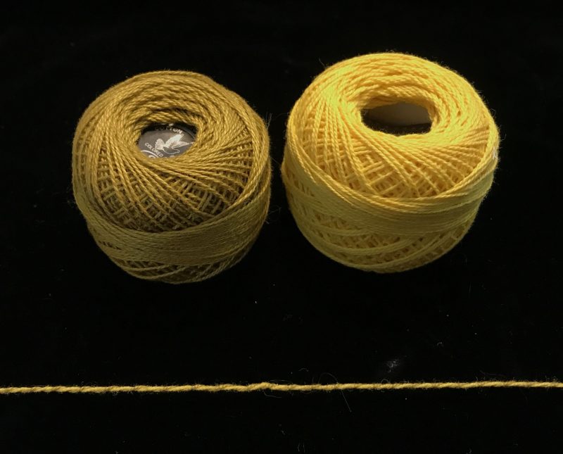 Two balls of yarn, yellow and olive, which twist together into a strand of nearly uniform color.